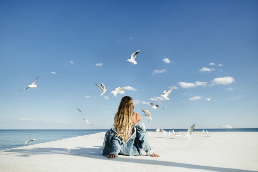 Girl is sitting on the berth and watching seagulls